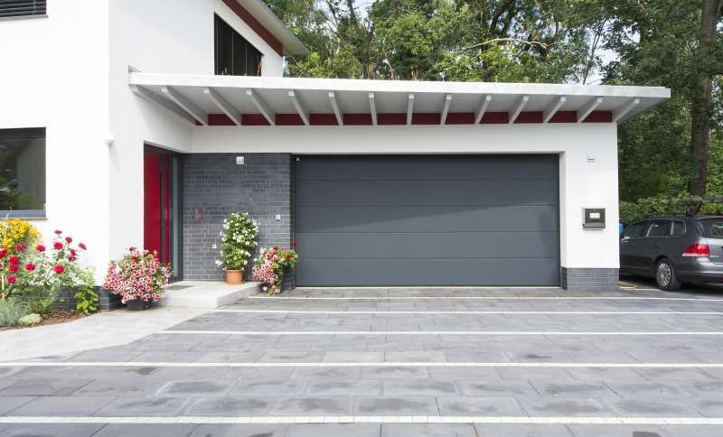 Vor einem Haus mit Garagentor ist ein Auto geparkt.