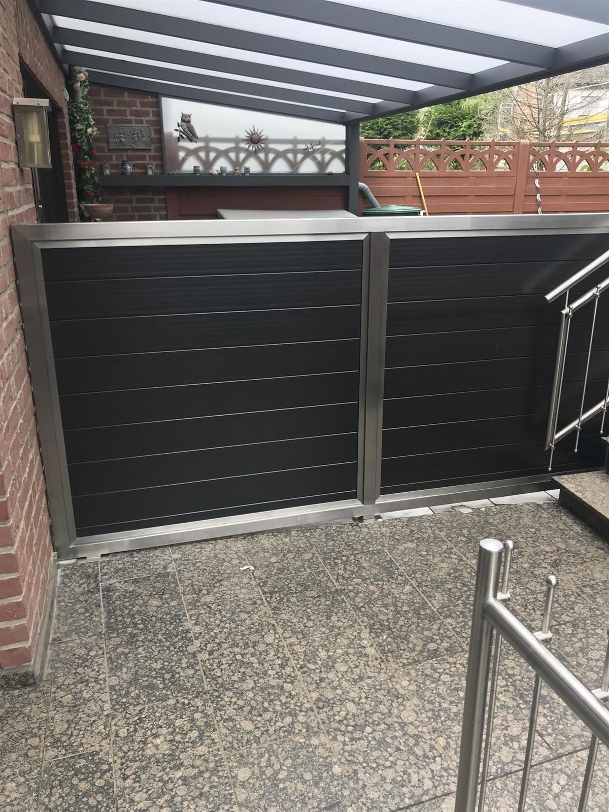 Vor einem Backsteingebäude steht ein schwarzer Zaun mit Edelstahlrahmen.