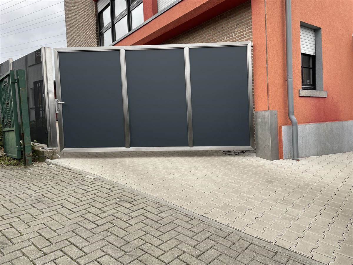 Vor einem roten Gebäude steht ein Edelstahltor.