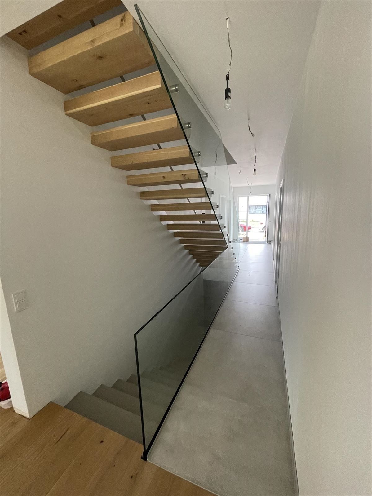 Eine Treppe mit Holzstufen und einem Glasgeländer in einem Flur.