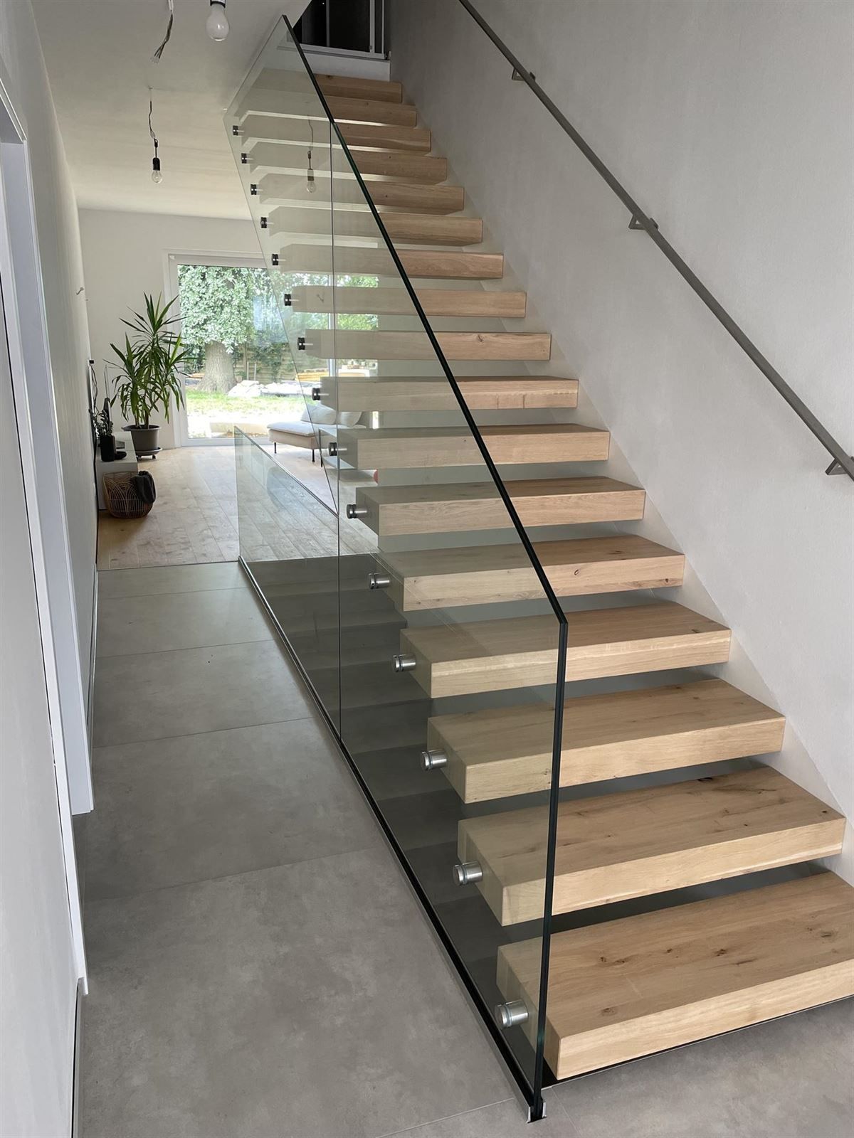 Eine Holztreppe mit einem Glasgeländer in einem Flur.