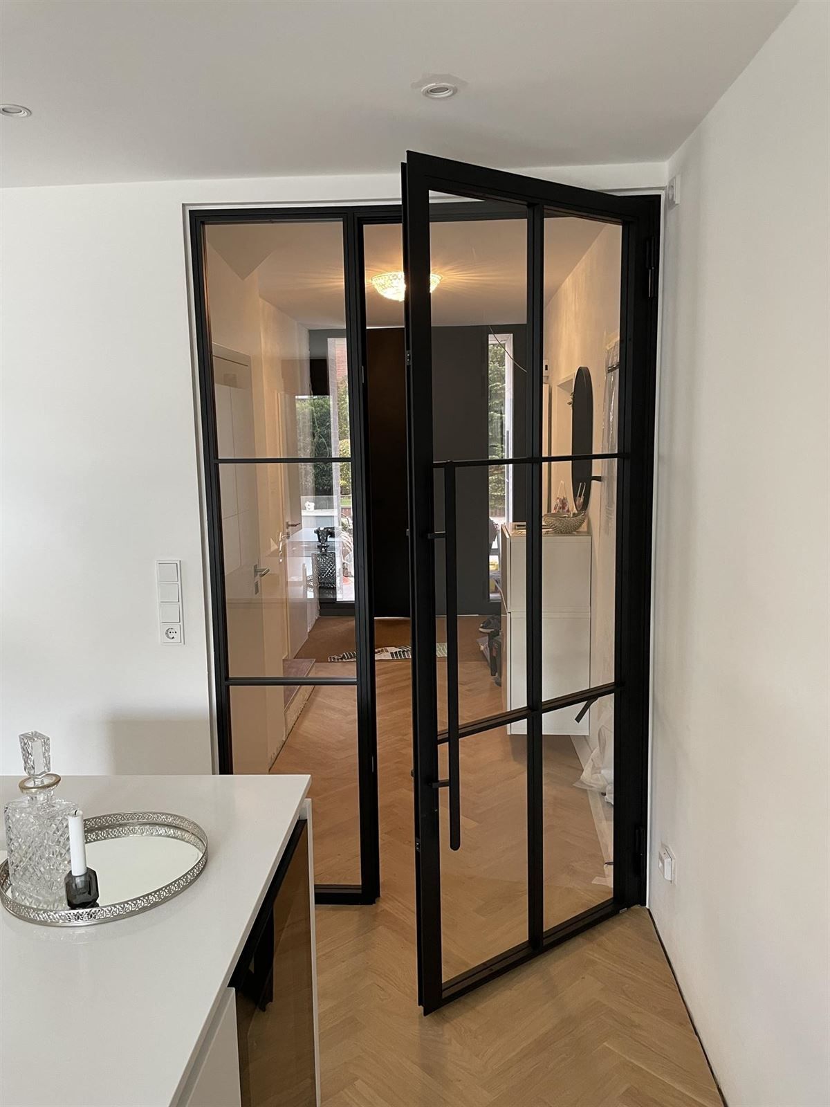 In einem Flur, der zu einem Wohnzimmer führt, ist eine Glastür offen.