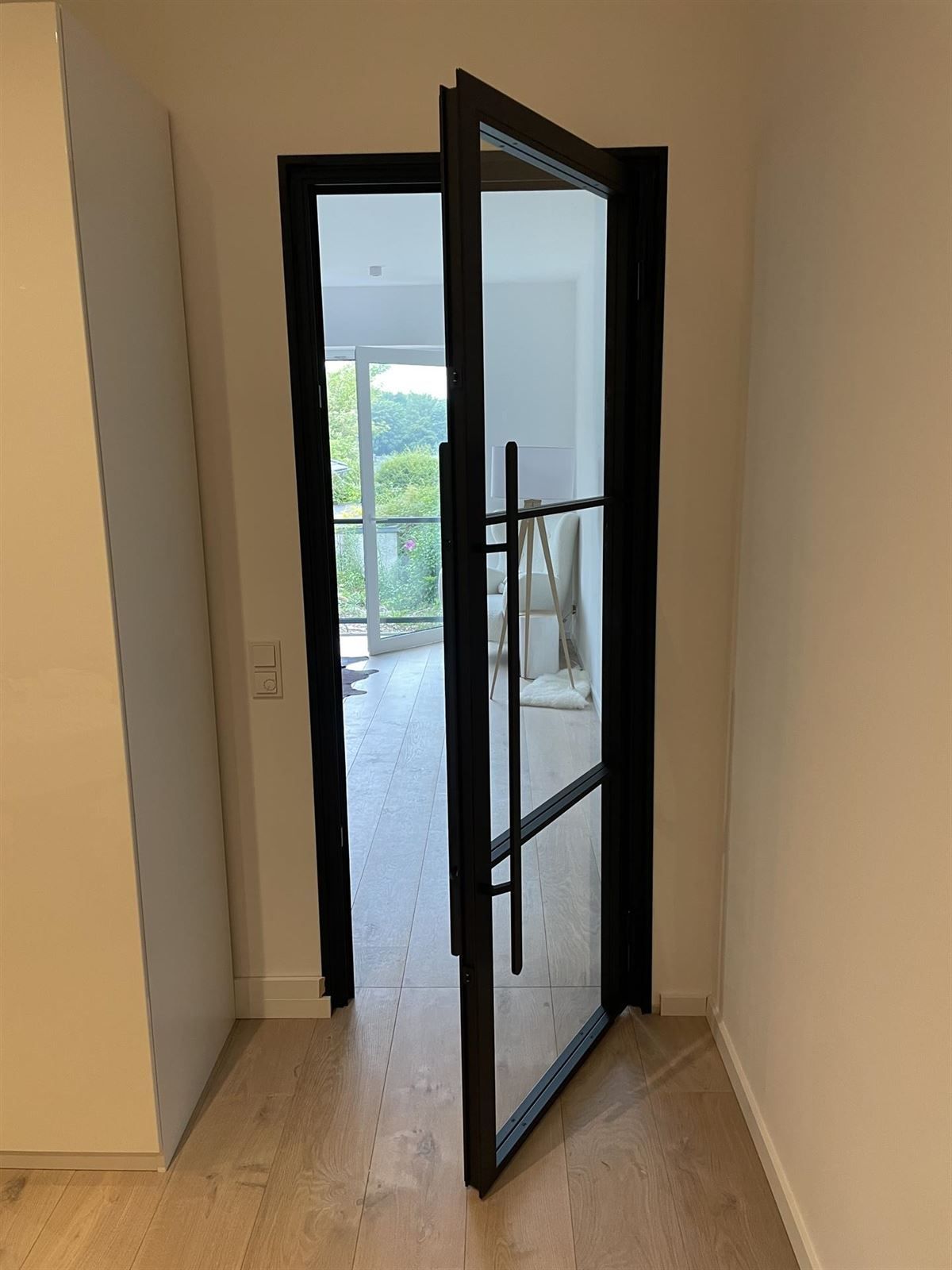 In einem Flur steht eine Tür mit schwarzem Rahmen und Glas offen.