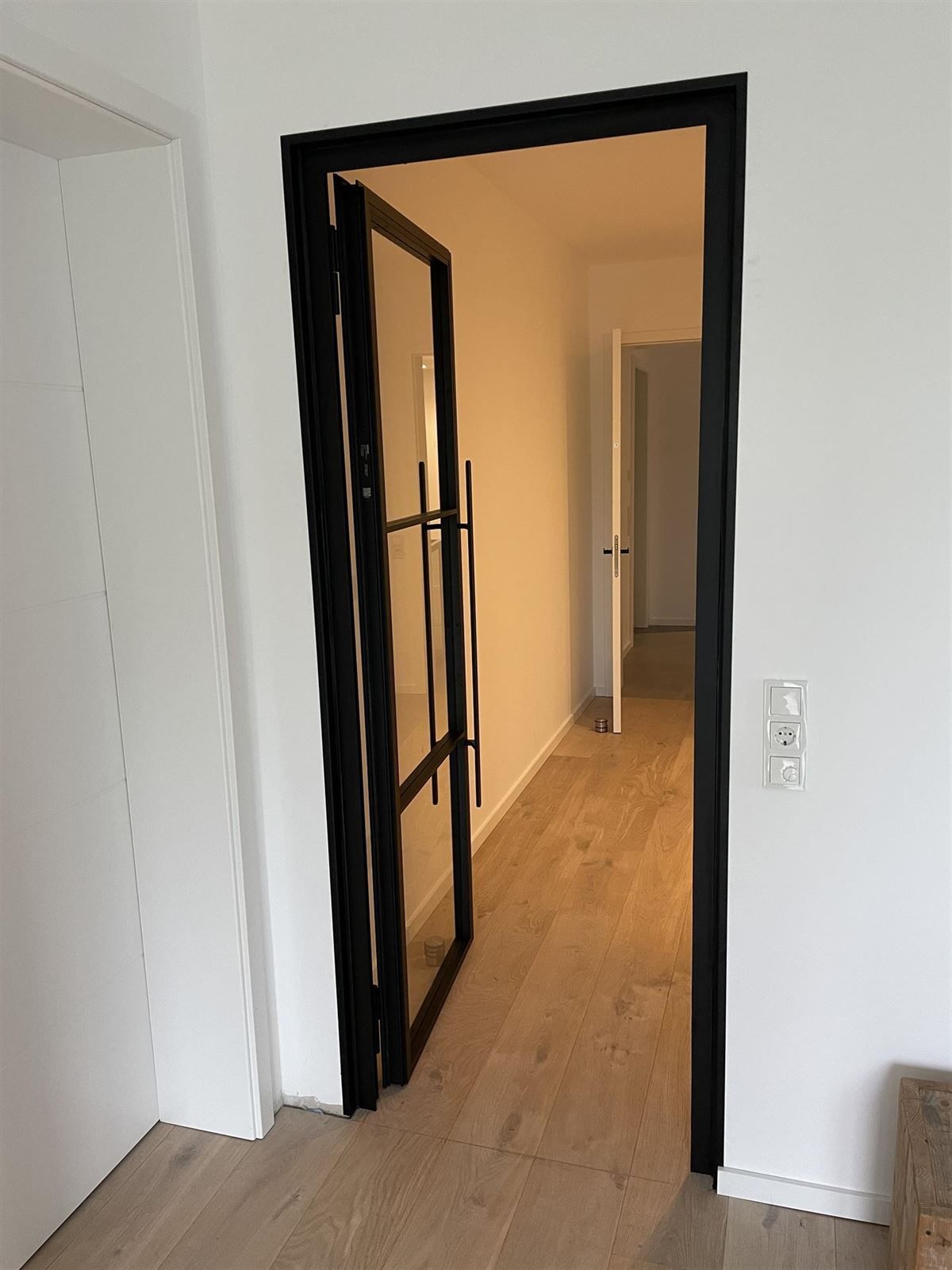 Ein Flur mit einer schwarzen Tür und einem Holzboden.