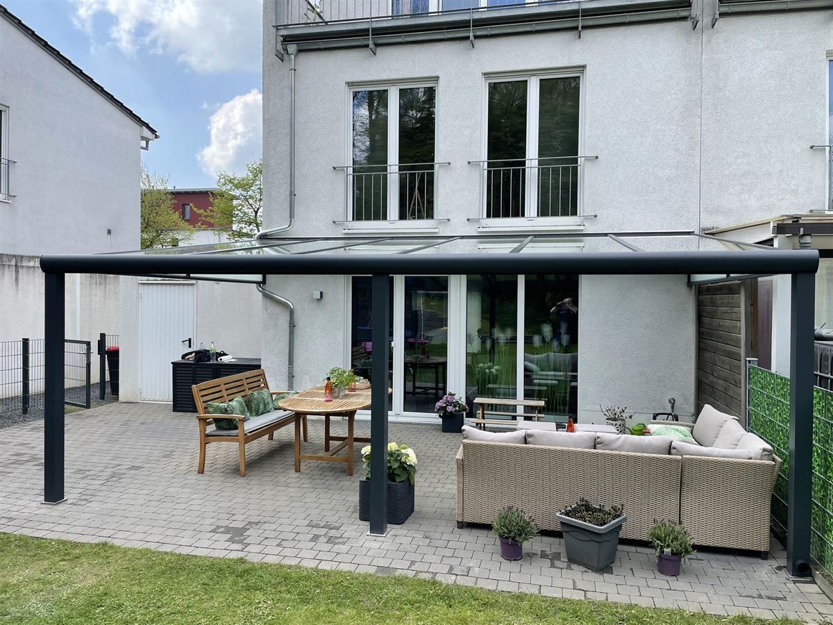 Eine Terrasse mit einem Baldachin darüber und einem Tisch und Stühlen vor einem Haus.