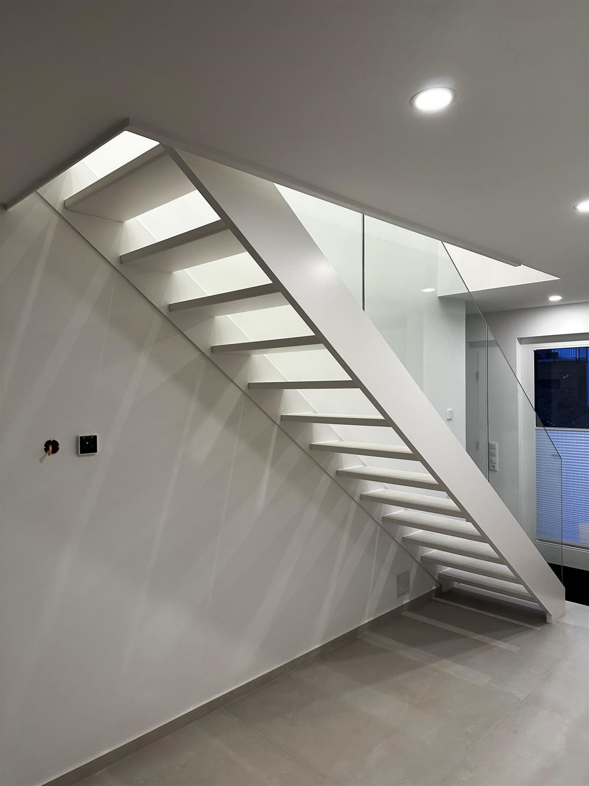 Eine weiße Treppe mit einem Glasgeländer in einem Raum.