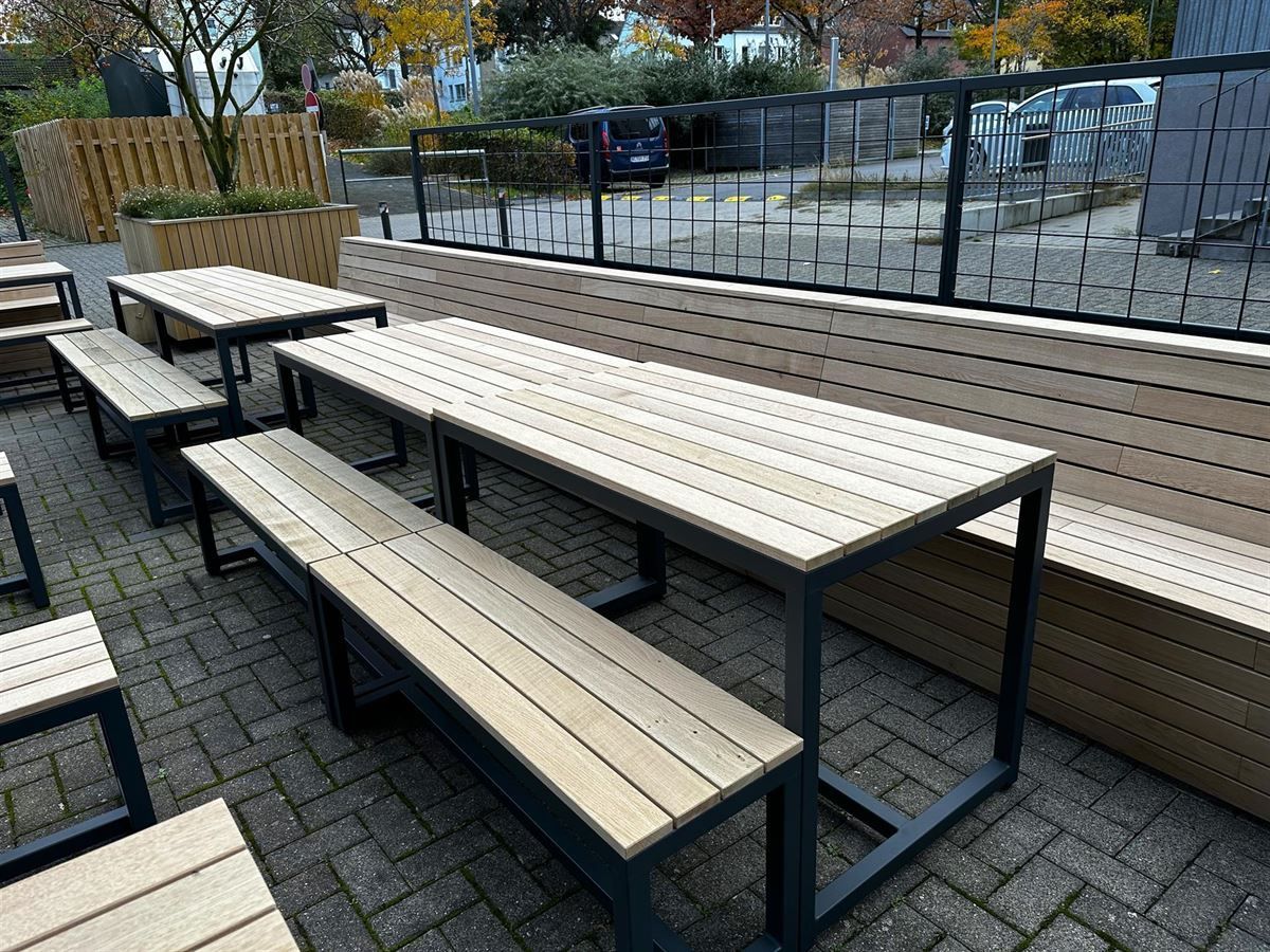 Eine Reihe von Holztischen und Bänken auf einem gepflasterten Gehweg.