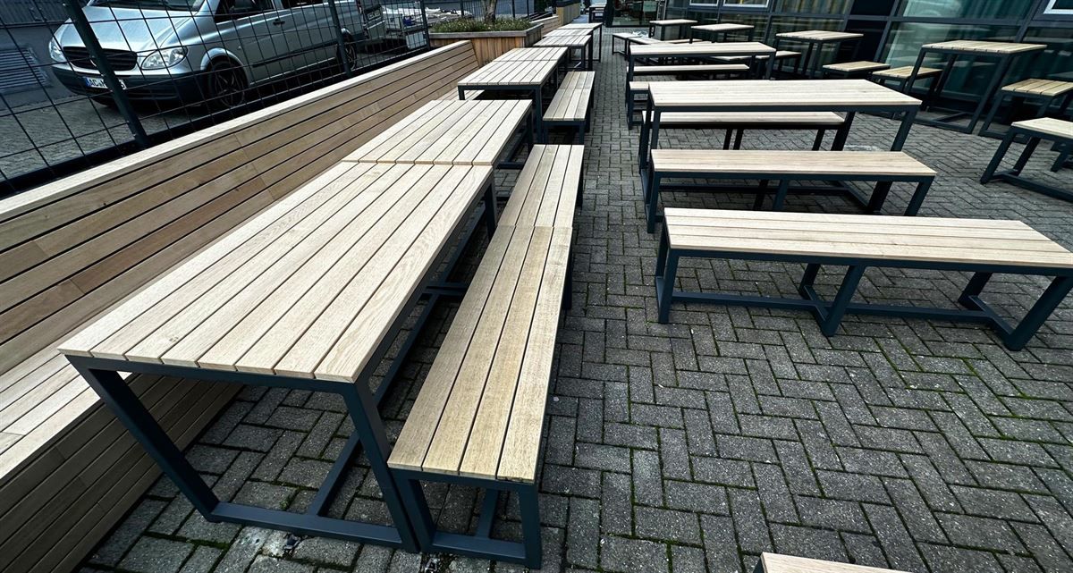 Eine Reihe von Holztischen und Bänken auf einem gepflasterten Gehweg.