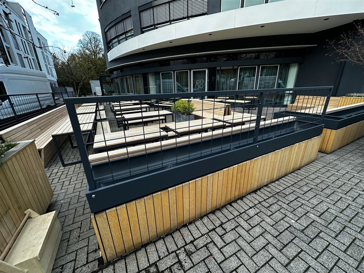 Ein gemauerter Gehweg führt zu einem Restaurant mit einem hölzernen Blumenkasten und einem Metallgeländer.