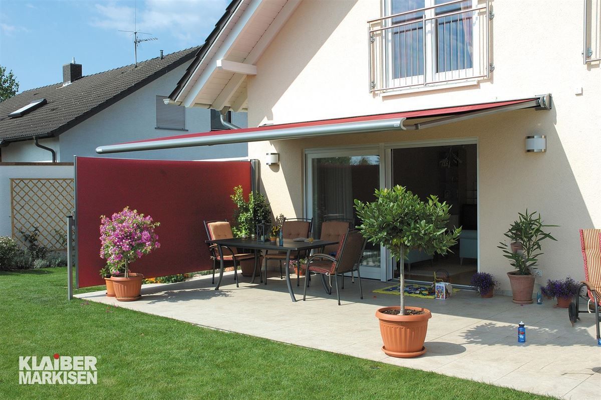 Ein Haus mit einer Terrasse mit Tisch und Stühlen unter einer Markise