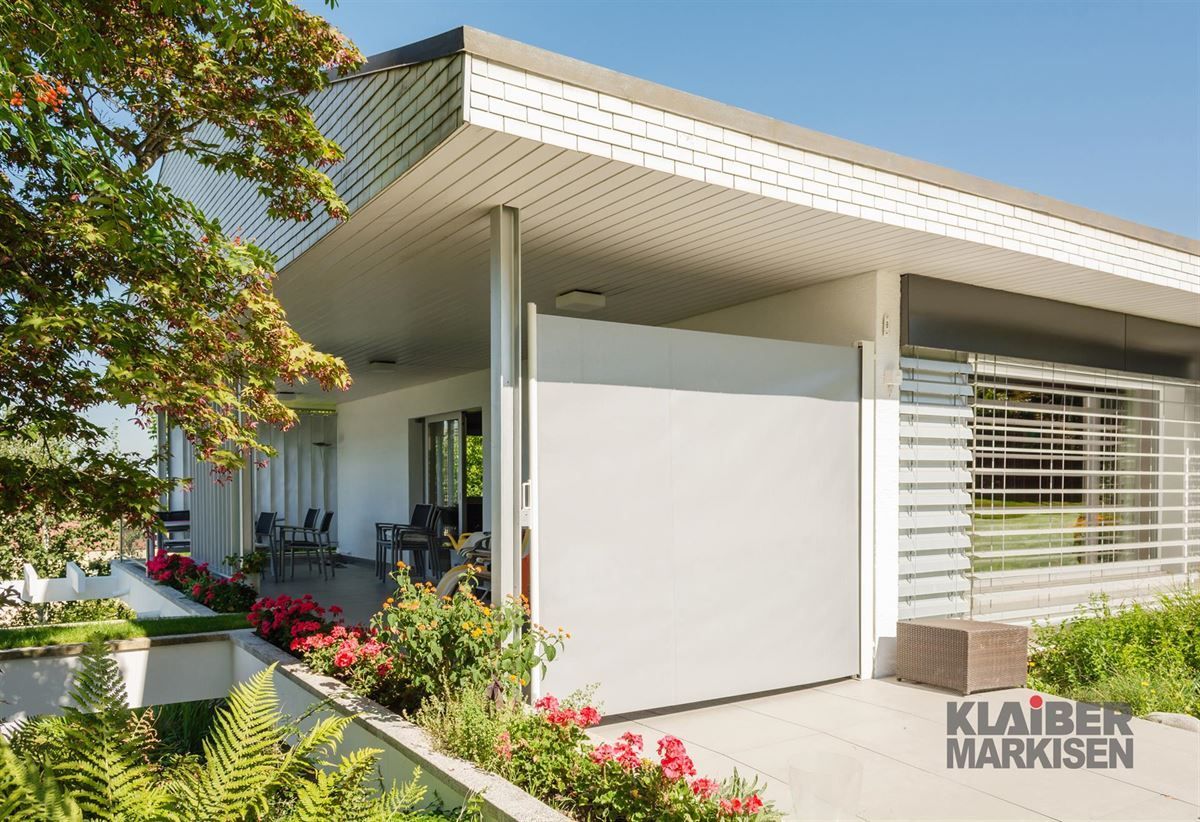 Ein weißes Haus mit einer Terrasse und Blumen davor