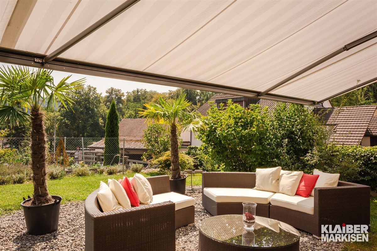 Eine Terrasse mit Couch, Stühlen und Tisch unter einer Markise.
