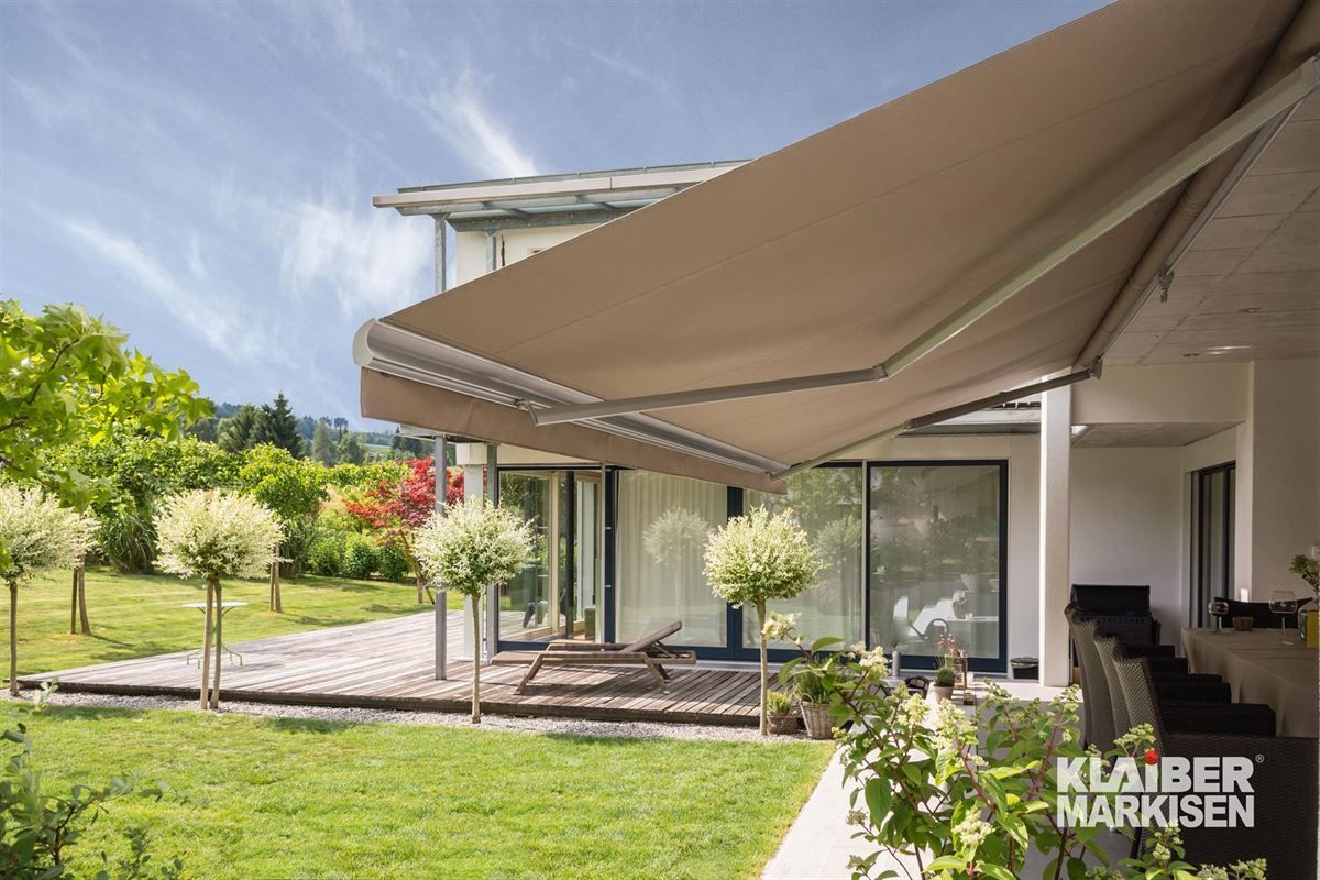 Eine große Markise überdacht eine Terrasse vor einem Haus.