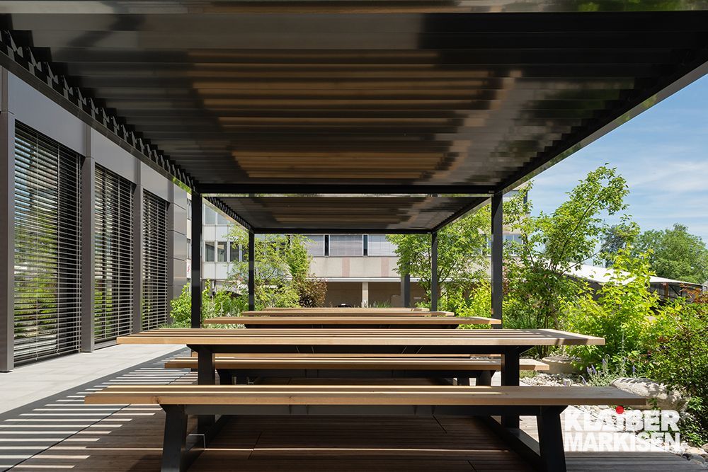 Eine Reihe hölzerner Picknicktische unter einem Baldachin.