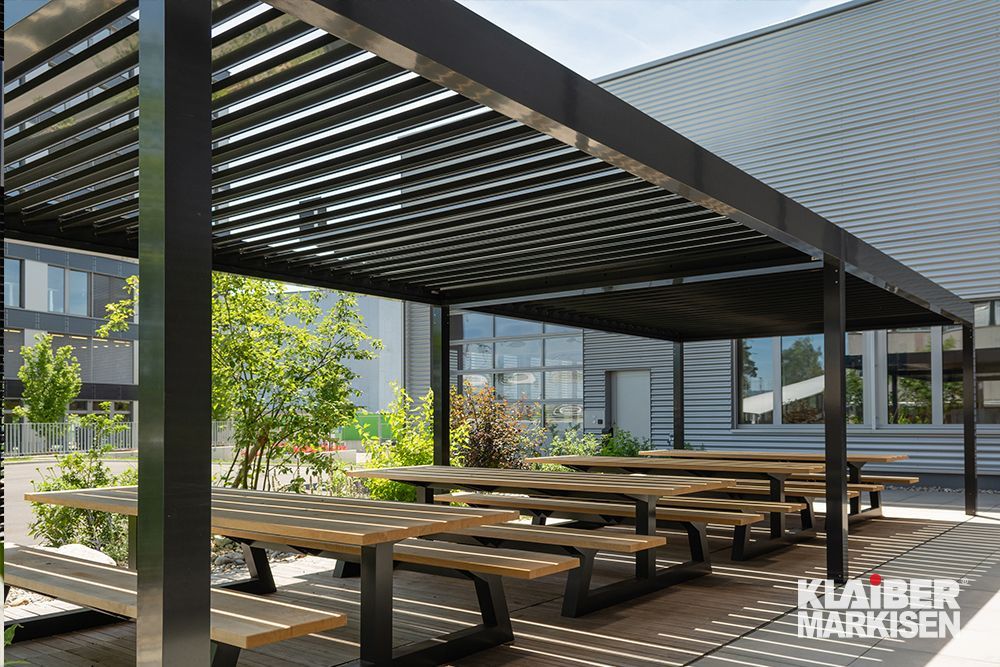 Eine Reihe hölzerner Picknicktische unter einer Pergola.