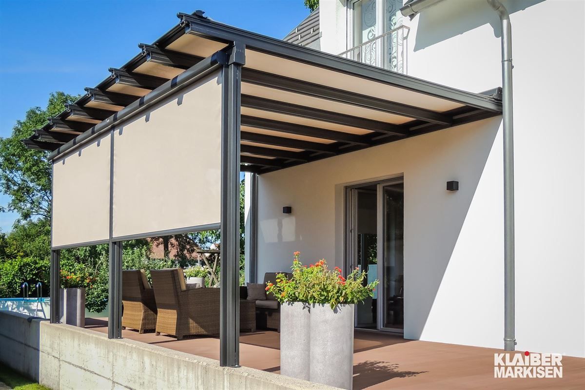 Eine Terrasse mit Pergola und einem Esstisch und Stühlen darunter.