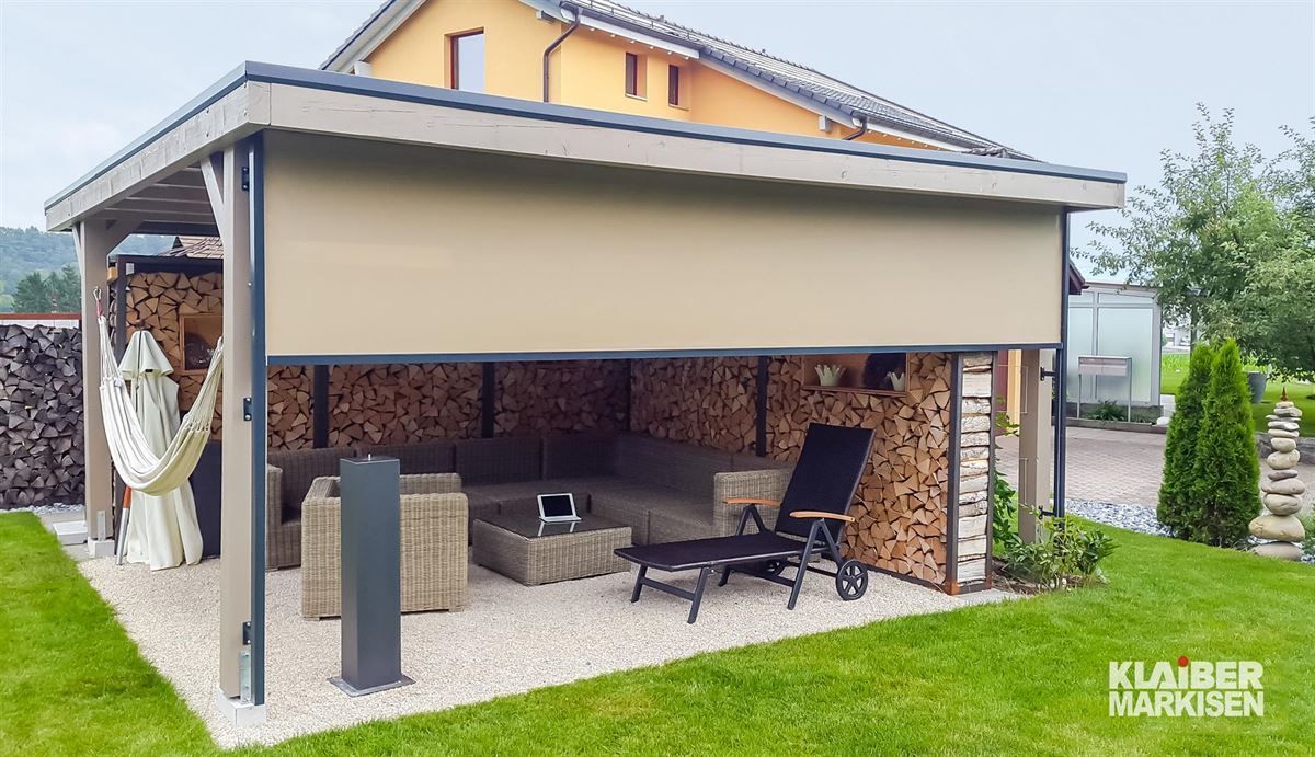 Eine Pergola mit Sofa, Stühlen und Hängematte vor einem Haus.