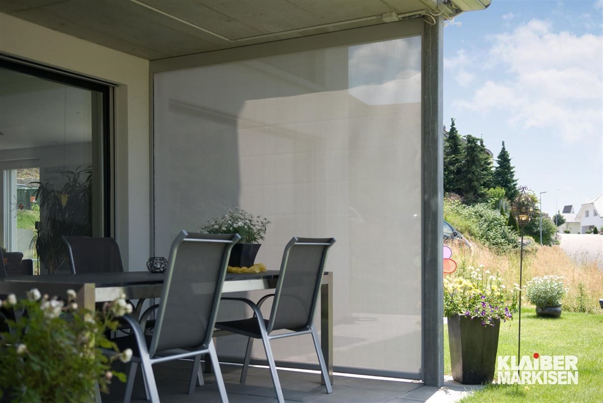 Eine Terrasse mit Tisch und Stühlen und einem Sichtschutz zwischen Tisch und Stühlen.