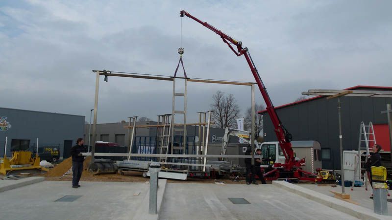 Ein roter Kran hebt eine Metallkonstruktion auf einem Parkplatz an