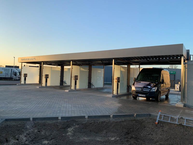 Ein blauer Lieferwagen steht unter einem Vordach einer Autowaschanlage.