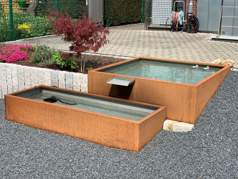 Auf einer Kiesauffahrt stehen einige mit Wasser gefüllte Behälter.