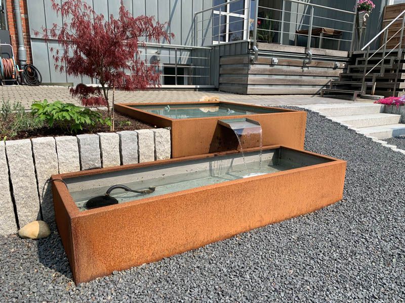 Auf einer Kiesauffahrt vor einem Gebäude steht ein Springbrunnen.