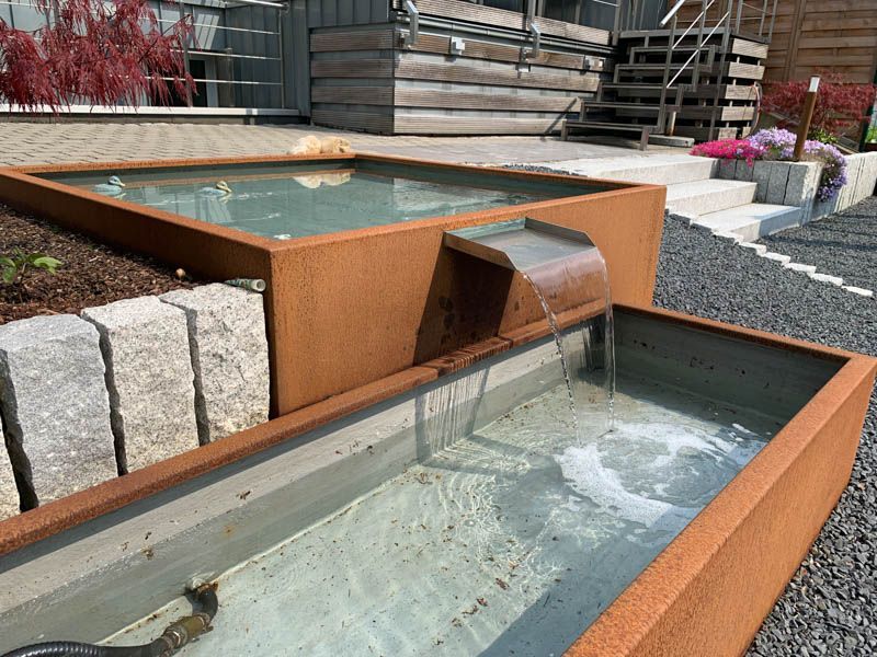 Ein Springbrunnen in einem Garten mit einer Treppe im Hintergrund.