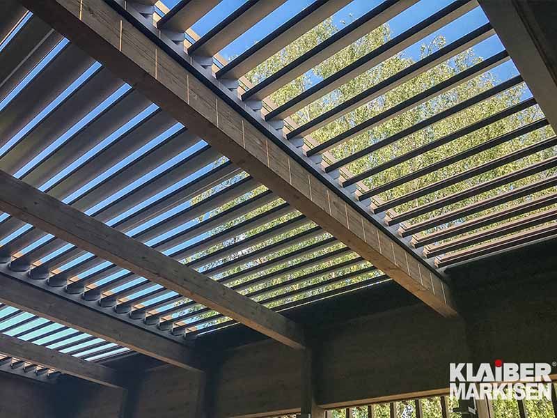 Blick nach oben zur Decke einer Pergola mit einem blauen Himmel im Hintergrund.