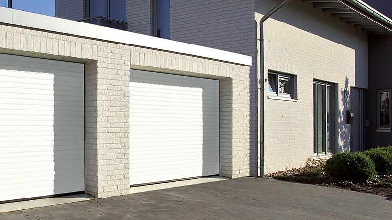 Vor einem Haus stehen zwei weiße Garagentore nebeneinander.