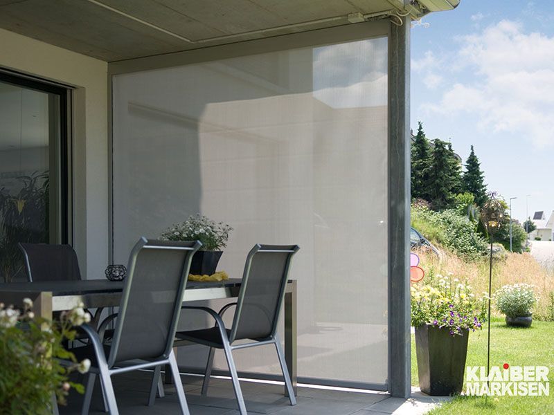 Eine Terrasse mit Tisch und Stühlen und einem Sichtschutz zwischen Tisch und Stühlen.