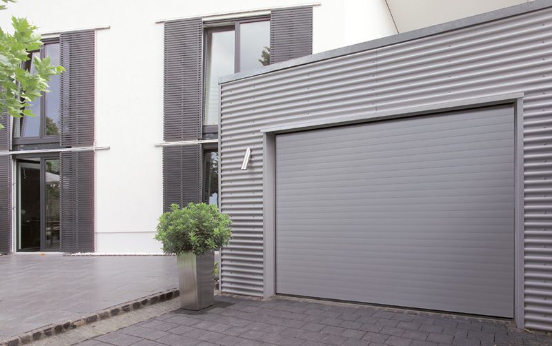 Vor einem weißen Haus steht ein graues Garagentor offen.