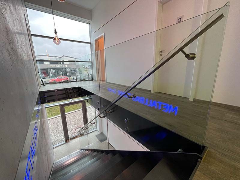 Eine Treppe mit Glasgeländer und blauem Licht an der Wand.
