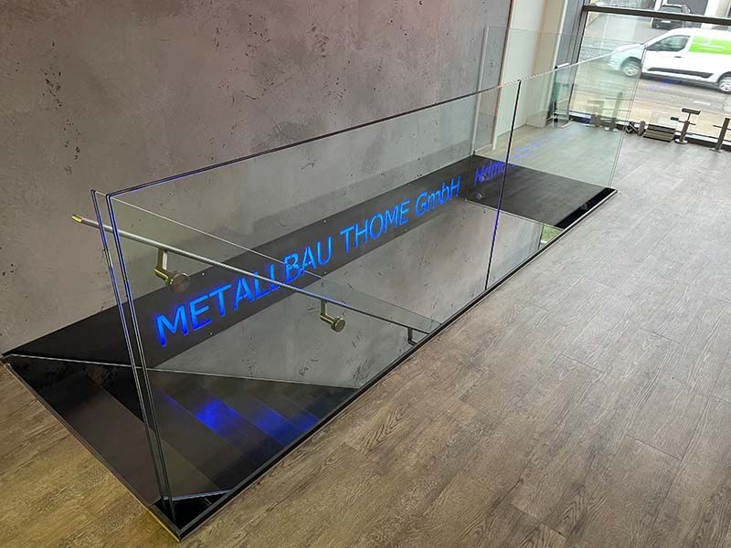 Eine Treppe mit einem Glasgeländer und einem Schild mit der Aufschrift „Metal Rau Thompson“.