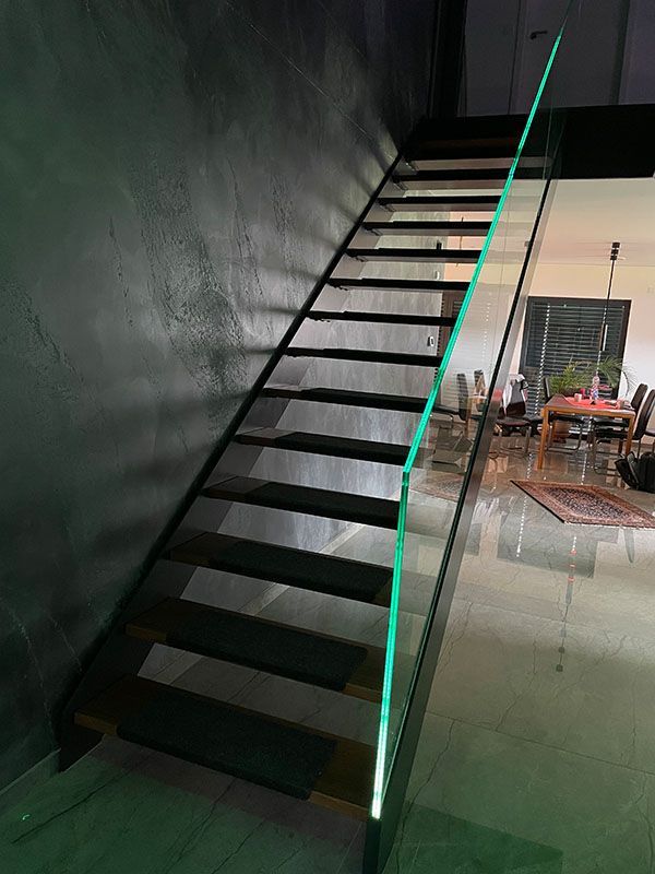 Eine schwarze Treppe mit einem Glasgeländer in einem Wohnzimmer.