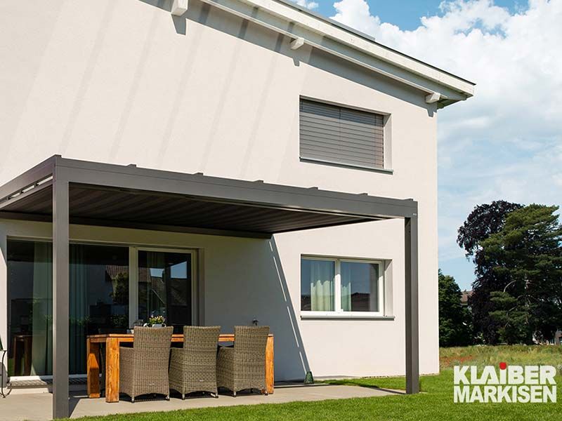 Ein weißes Haus mit einer Terrasse mit Tisch und Stühlen unter einer Pergola.