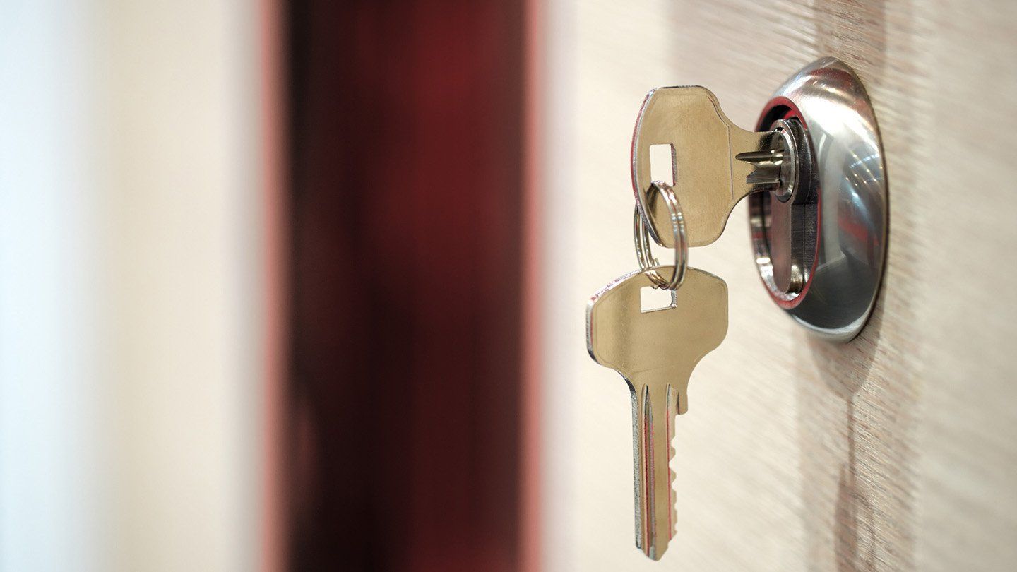 Una llave plateada insertada en una cerradura metálica, con una segunda llave colgando del llavero.