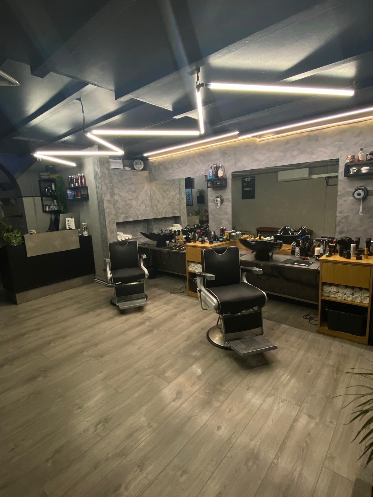 Vista interior de una barbería con dos sillas de barbero, espejos e iluminación moderna.