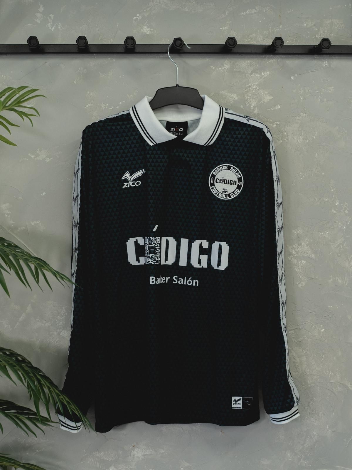 Camiseta de fútbol negra de manga larga colgada en un perchero. Tiene cuello y mangas blancos y logotipos de patrocinadores.