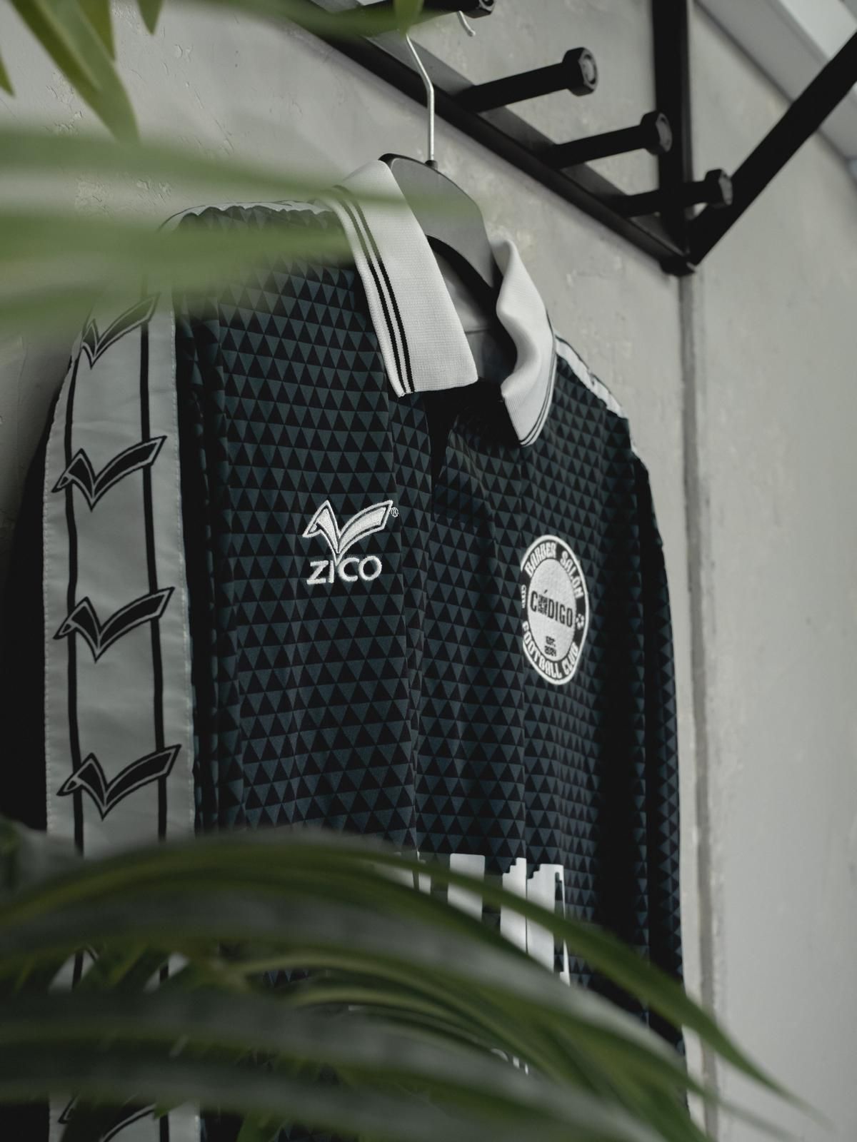 Camiseta de fútbol negra con detalles blancos, colgada en un perchero. Logotipo de Zico, escudo del equipo y diseños