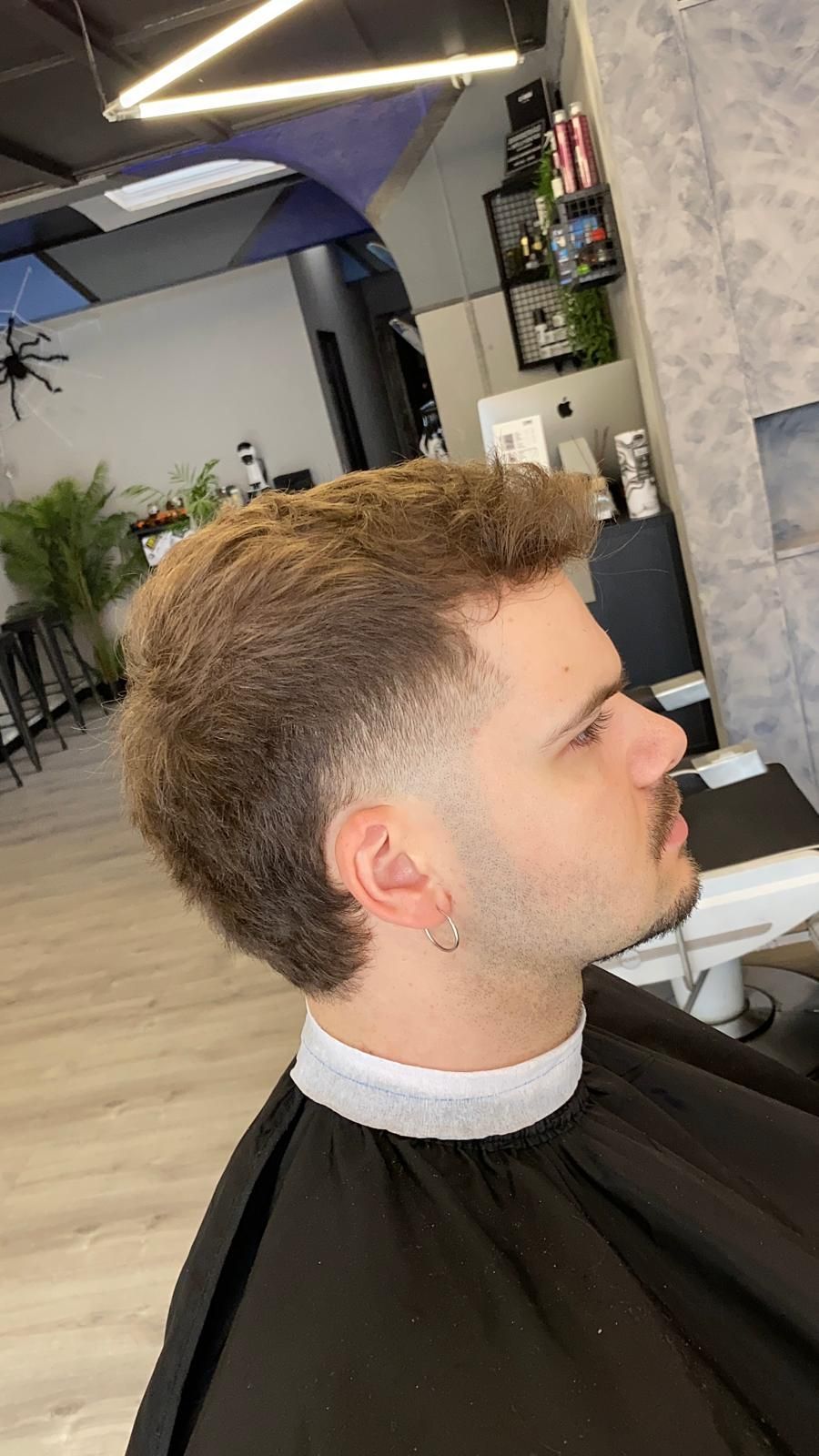 Hombre con corte de pelo degradado y perilla en un salón. Lleva una capa negra.