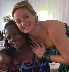 Deux femmes souriantes, l'une à la peau foncée tenant un bébé, l'autre à la peau claire, un bras autour d'elle