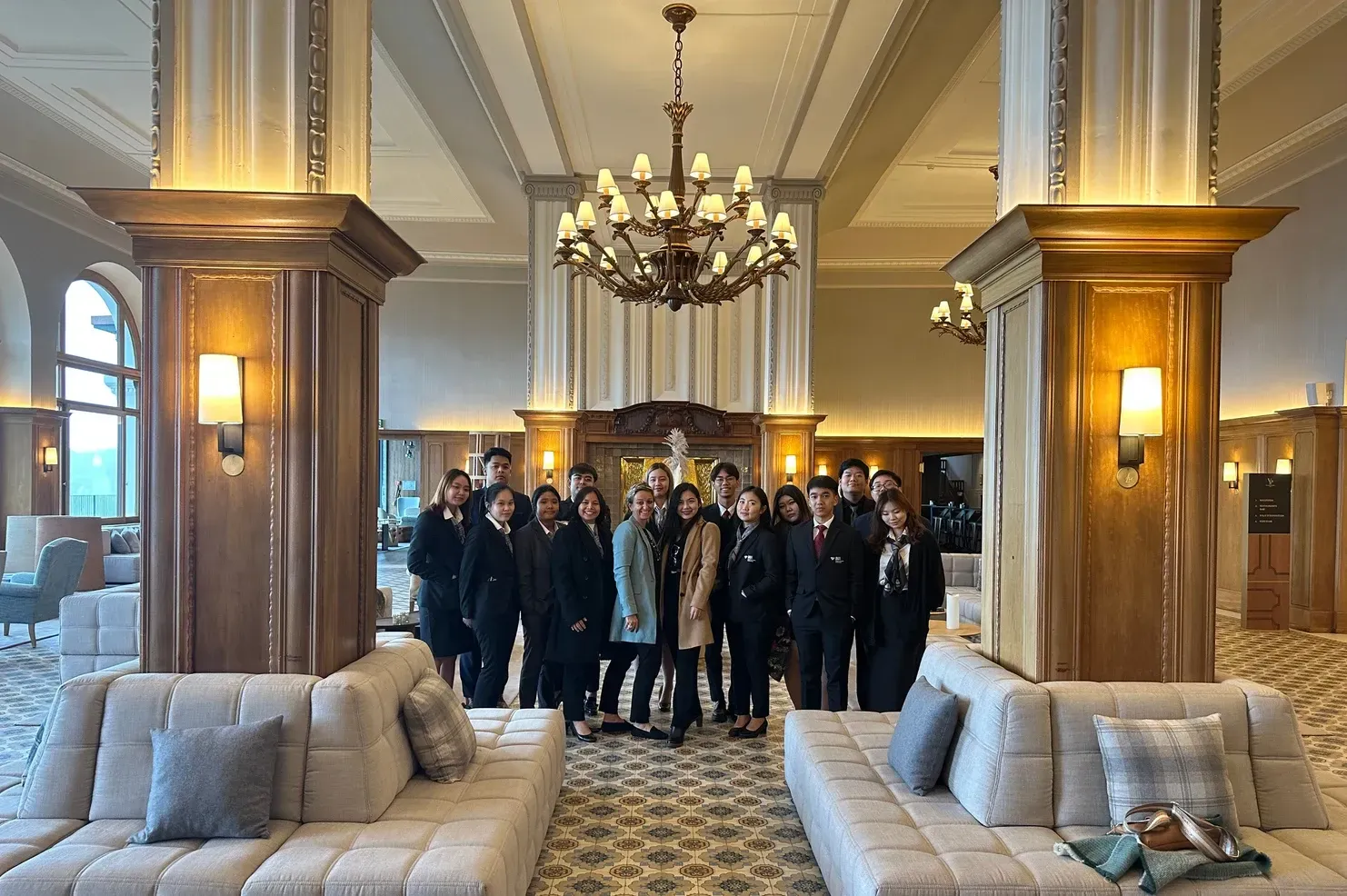 Un groupe de personnes pose dans le hall d'un hôtel avec deux grands canapés, des colonnes ornées et un lustre.