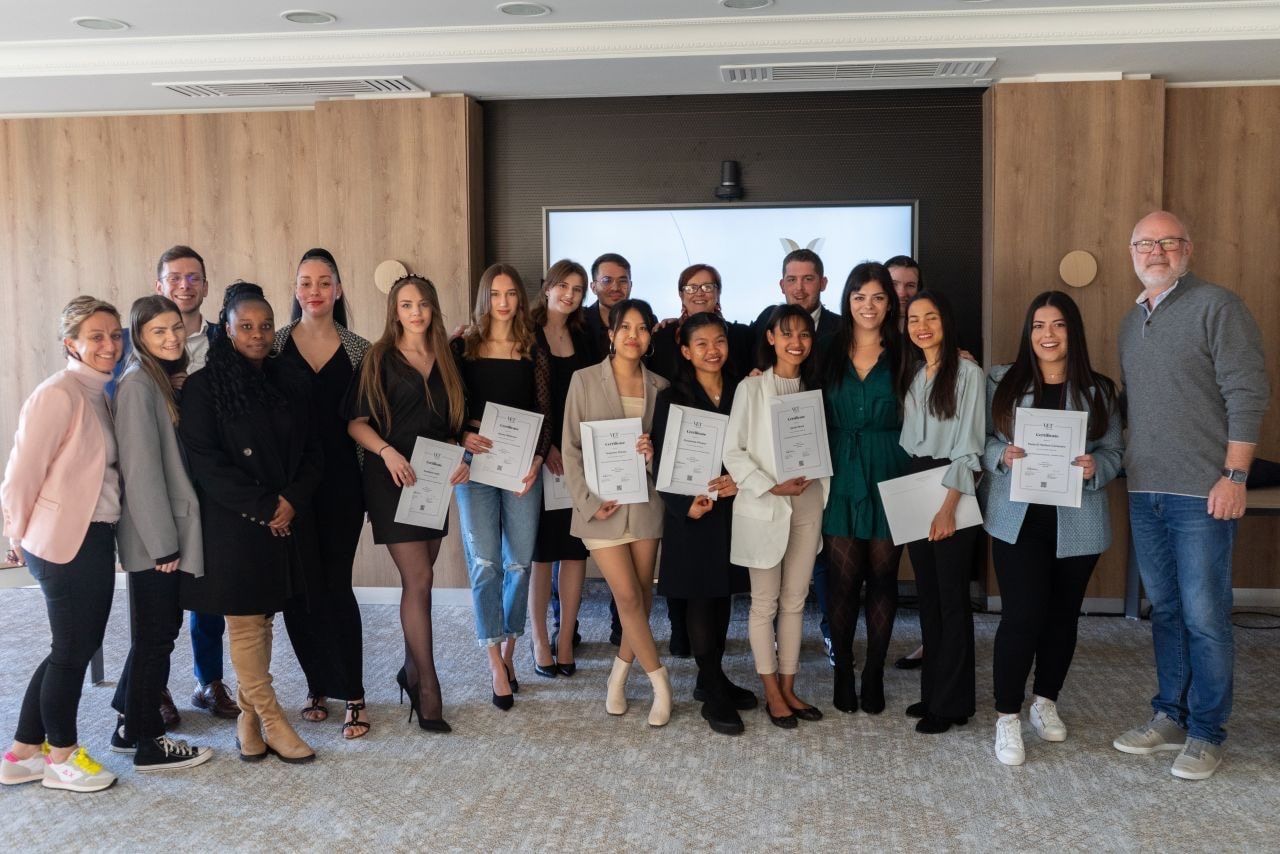 Groupe de personnes tenant des certificats dans une pièce lambrissée. Sourires et homme portant des lunettes.