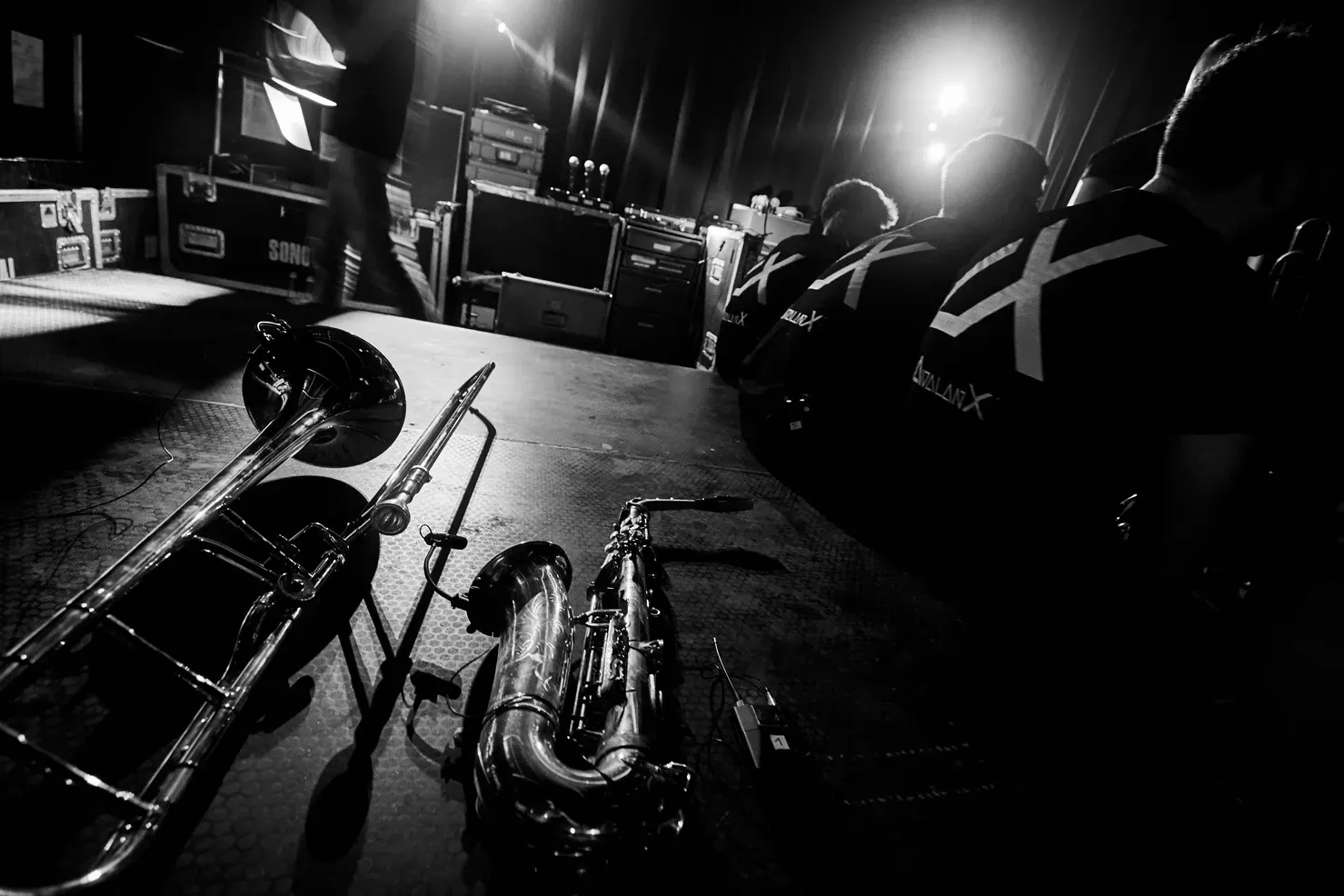 Trombone et saxophone sur scène avec un groupe en arrière-plan, les lumières de la scène s'allument.
