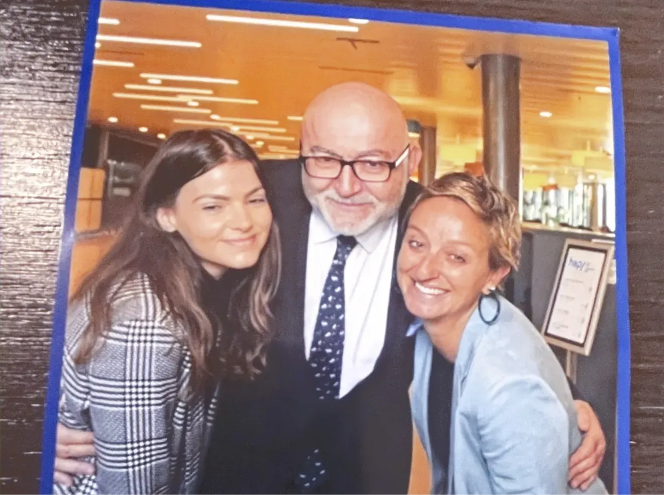 Trois personnes souriantes pour une photo à l'intérieur. Un homme en costume entouré de deux femmes.