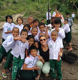 Un groupe d'enfants souriants en uniformes scolaires et une femme posent à l'extérieur.