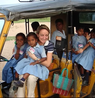 En Inde, une femme tient une fille sur ses genoux dans un pousse-pousse jaune ; des enfants en uniformes bleus sont présents.