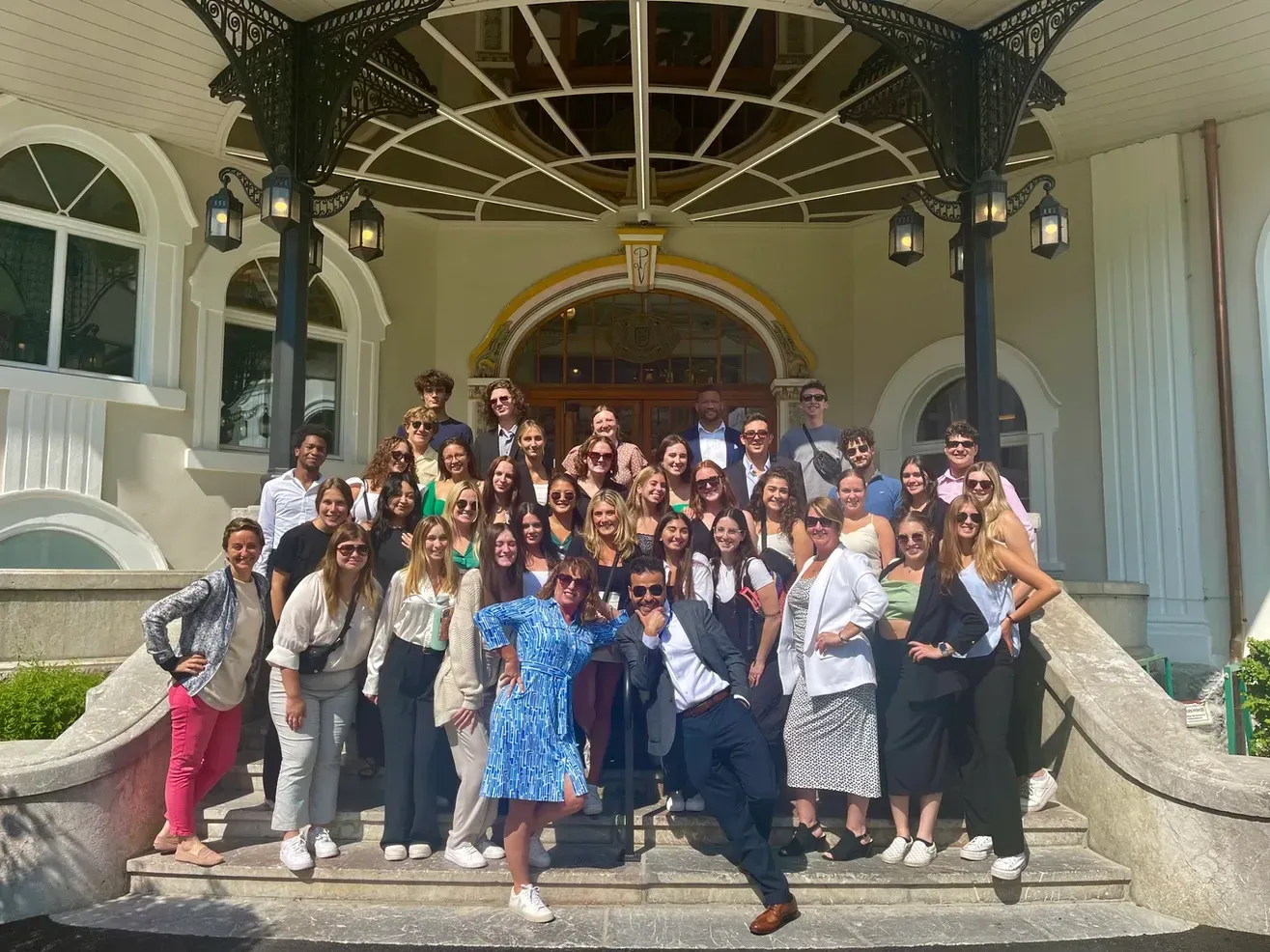 Groupe de jeunes posant sur les marches d'un immeuble avec une arche décorative. Soleil, sourires, tenues estivales.