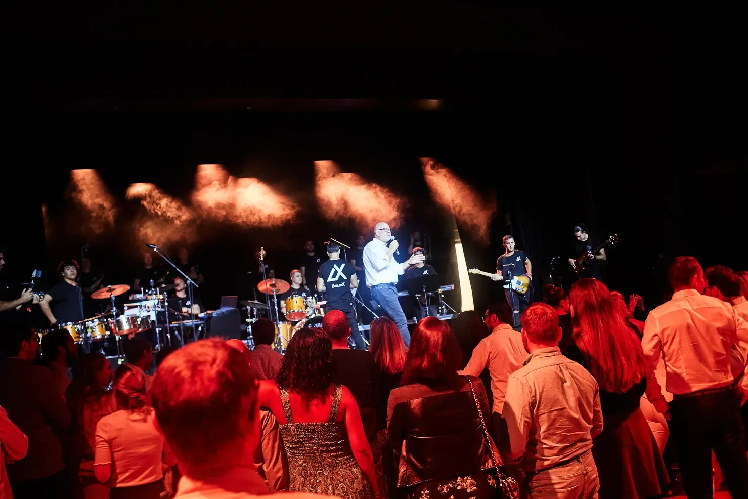 Groupe de musique se produisant sur scène sous des lumières rouges, avec un public au premier plan.
