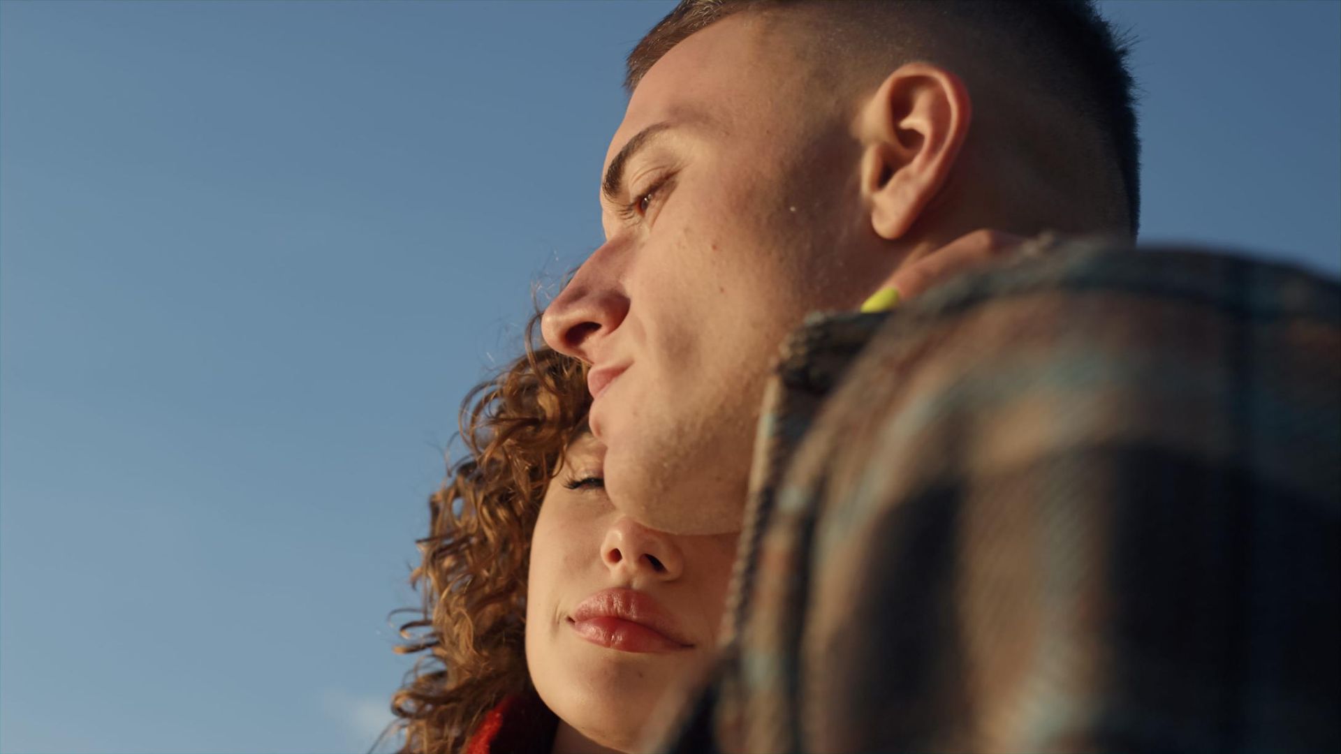 Dos personas con los ojos cerrados se apoyan una contra la otra contra un cielo azul